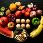 A slice of watermelon, a pomegranate (one whole, one halved), red apples, kiwis (whole and sliced), oranges, and a bunch of bananas.