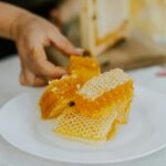Fresh honeycomb with golden raw honey on a white plate being cut by hand